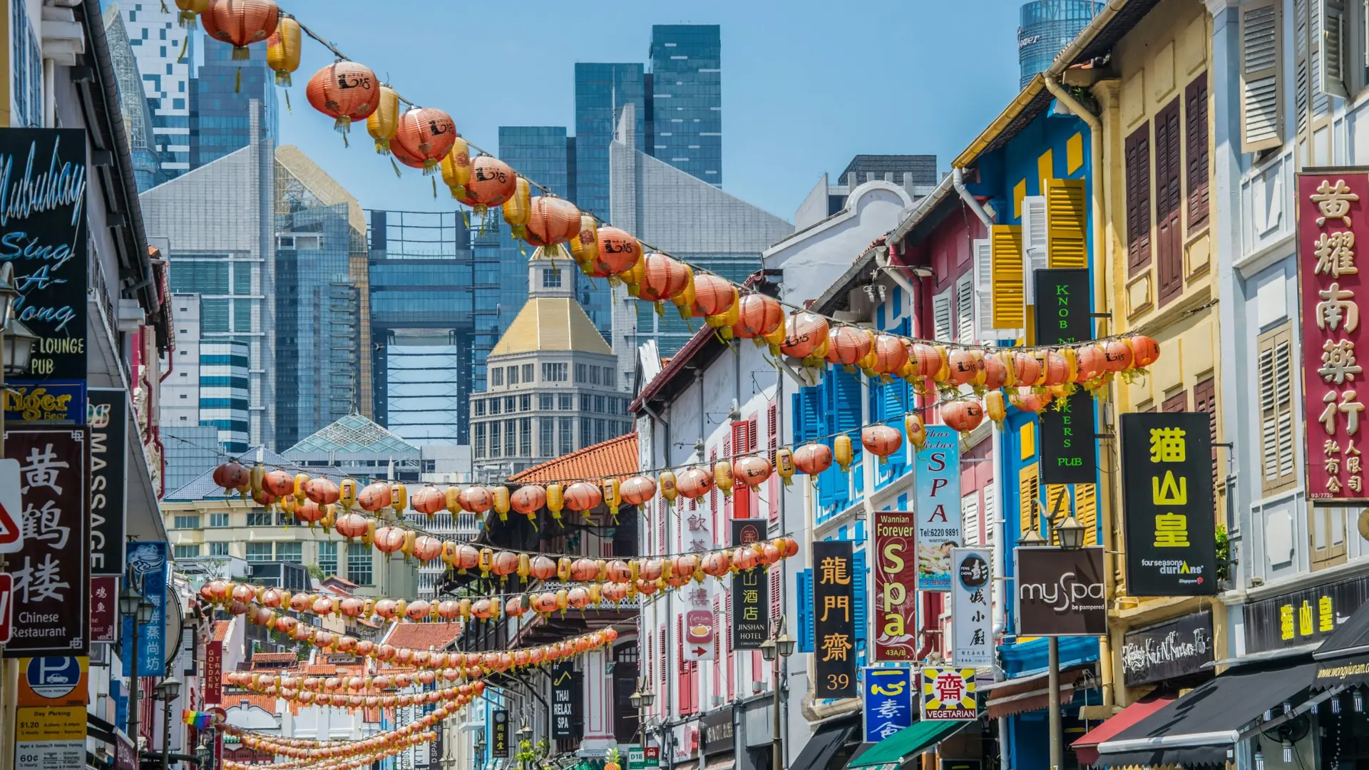 Strings of lanterns above a Chinatown street, with the skyscrapers of Singapore behind