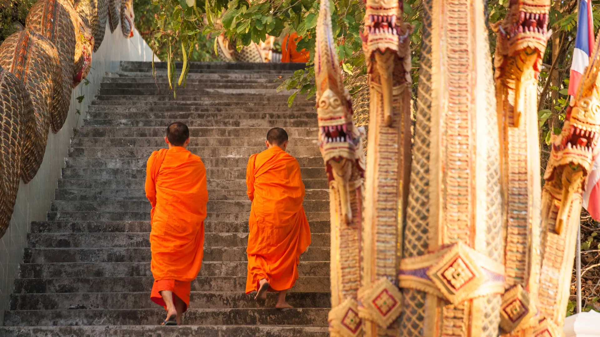 Two monks in orange robes climbing a staircase guarded by carved naga statues at Doi Suthep, Chiang Mai, Thailand
